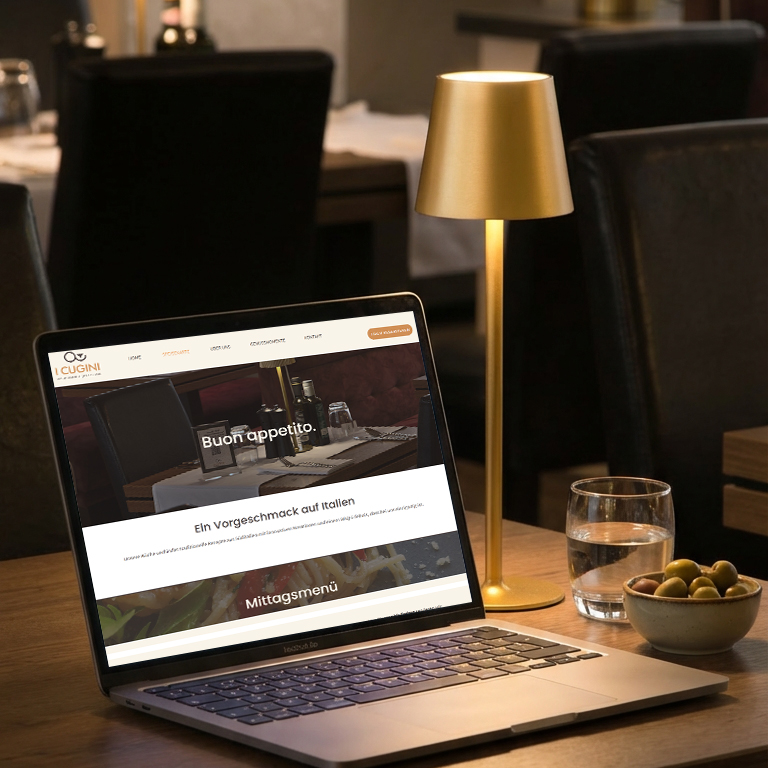 Laptop auf Holztisch mit geöffnetem Website-Design, Lampenlicht und Glas Wasser – Webdesign-Beispiel