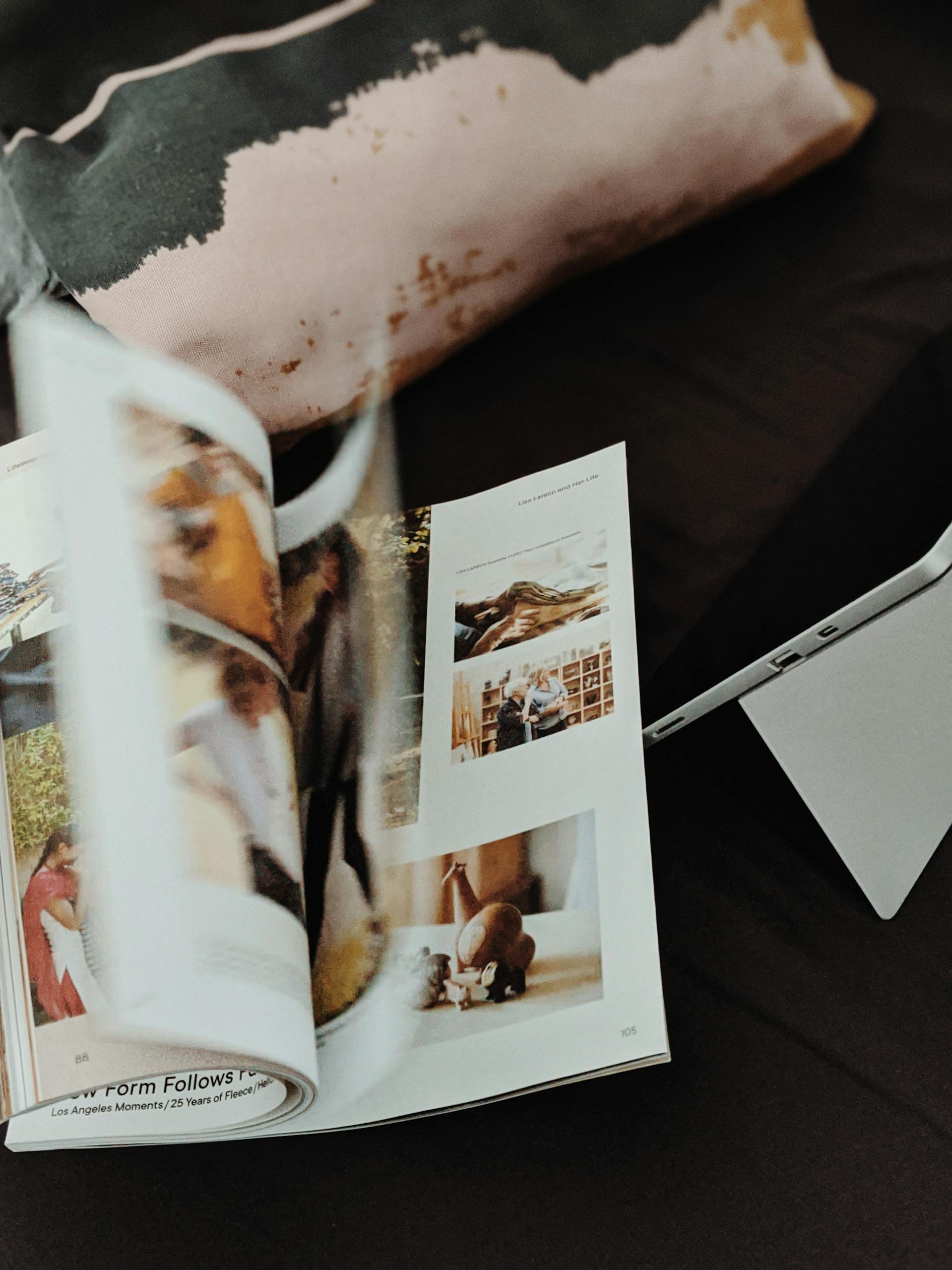 Close-up of an open magazine with blurred pages and a tablet on a dark surface.